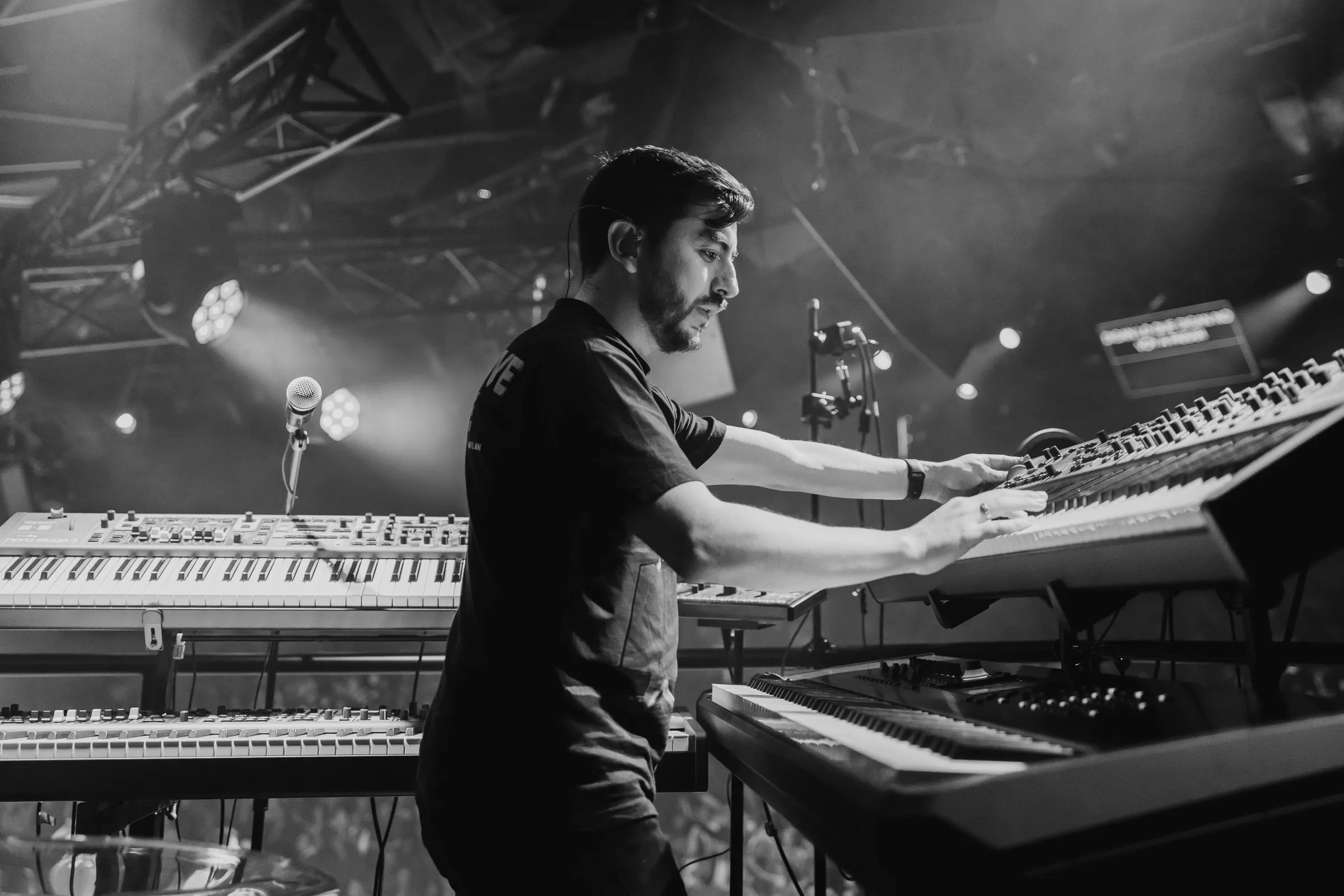 Sergio Bustos playing his Nord Stage rig under stage lighting, in black and white